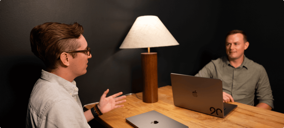 Two employees with their laptops having a conversation at a table.