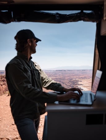 A man stands in front of a laptop while looking out in the distance