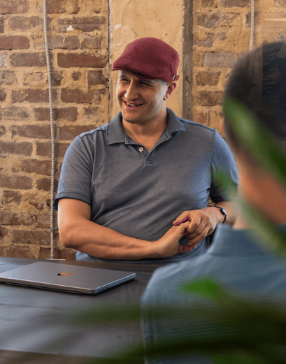 A man sits a table smiling at something out of frame