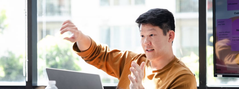 A man sits in front of a laptop while gesturing with his hands