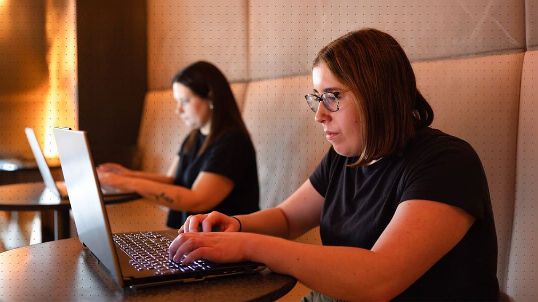 Two women sit side by side working on their laptops Two women sit side by side working on their laptops
