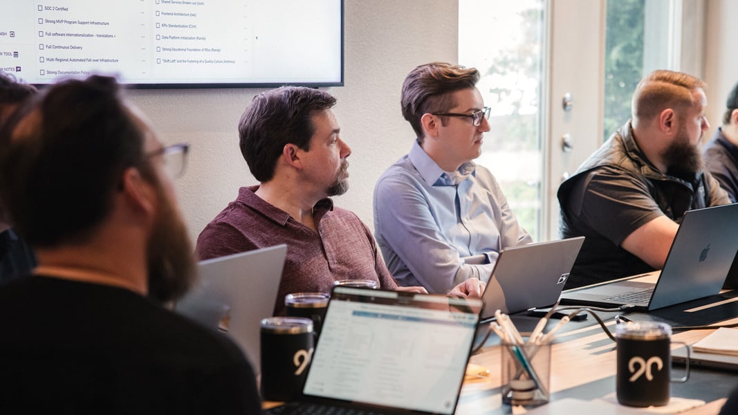 A group of men sit around a conference table with open laptops in front of them A group of men sit around a conference table with open laptops in front of them