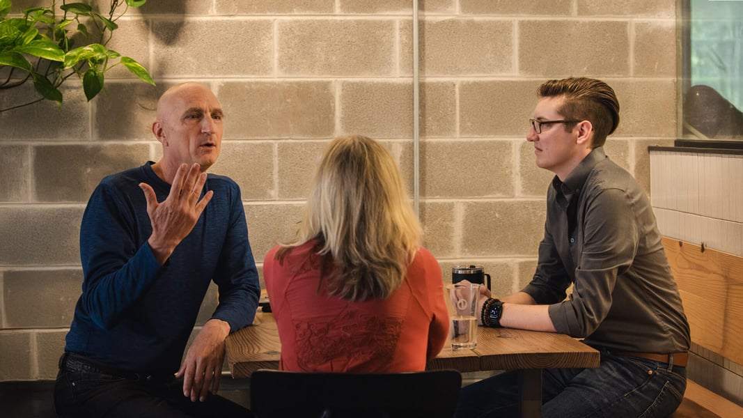 Three people sit at a table and talk.