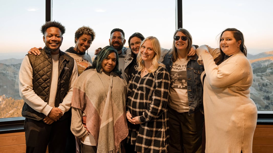 A group of eight people stands in front of a glass window smiling at the camera