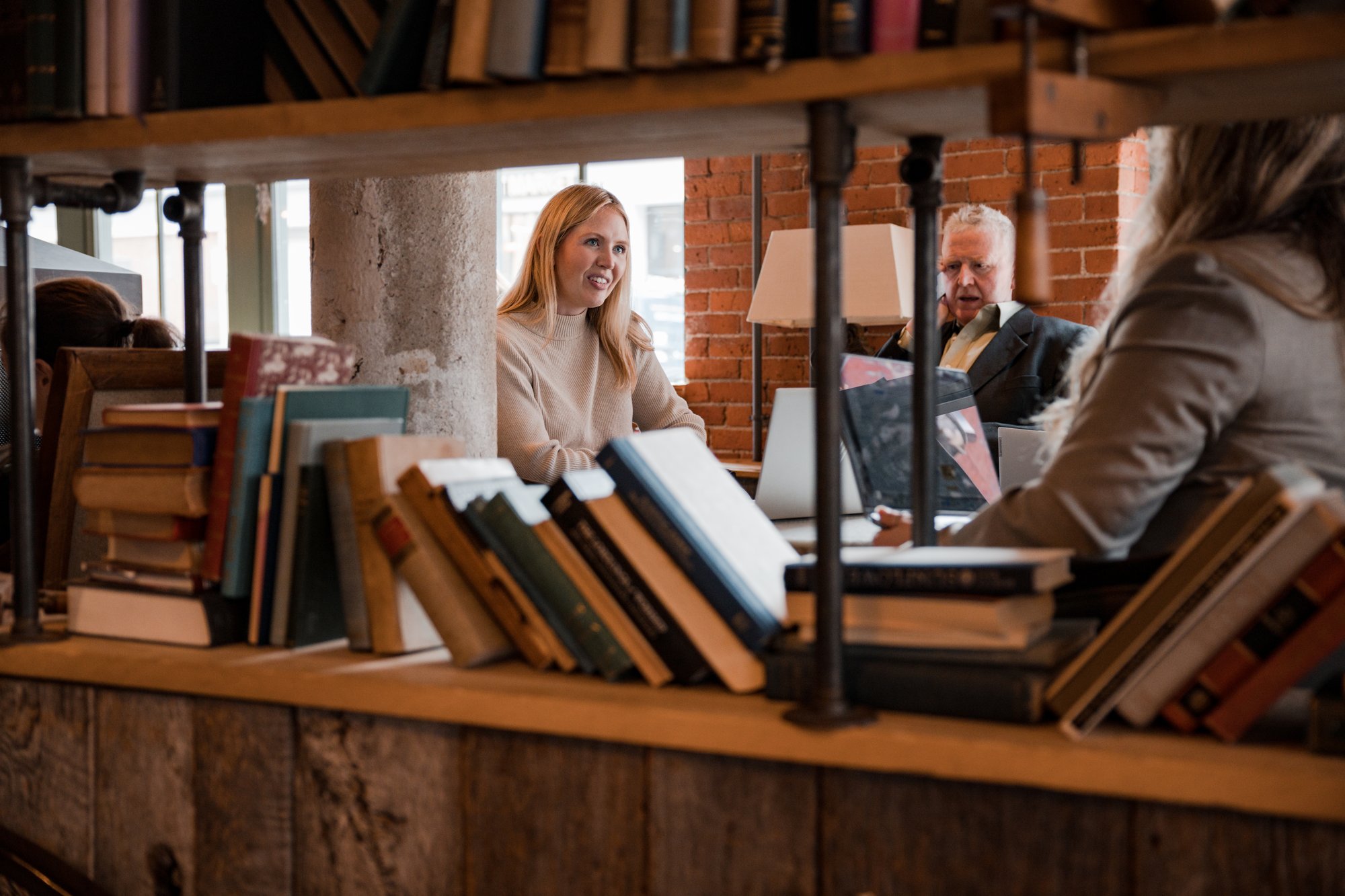 Two women and a man sit at a table behind a bookshelf.