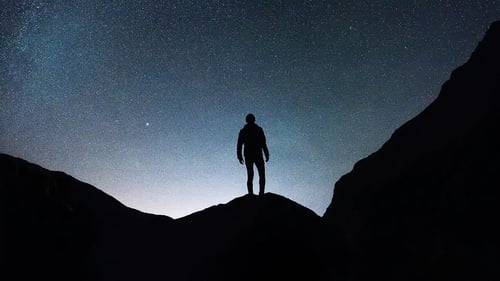 man standing on a mountain outlined against the night sky