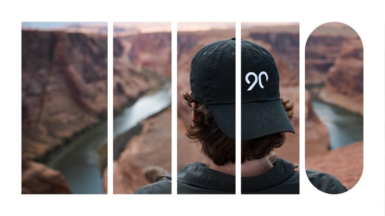 An individual wearing a 90 cap sitting on the edge of a canyon, looking down on a river.