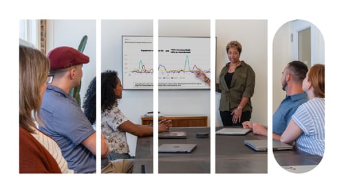 An employee giving a presentation with a slide deck behind her. Her colleagues are seated at a table in front of her and are looking on.