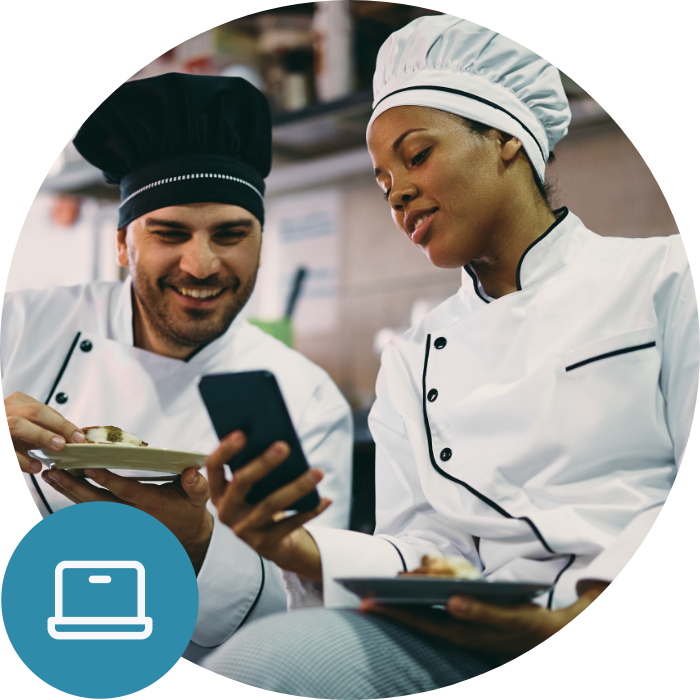 Two chefs standing in a kitchen looking at a phone Two chefs standing in a kitchen looking at a phone