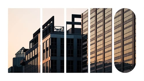 The exterior of an office building with glass windows illuminated by the sun during sunrise.