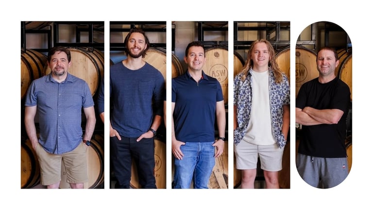 Ninety employees posing for a picture in front of beer barrels.