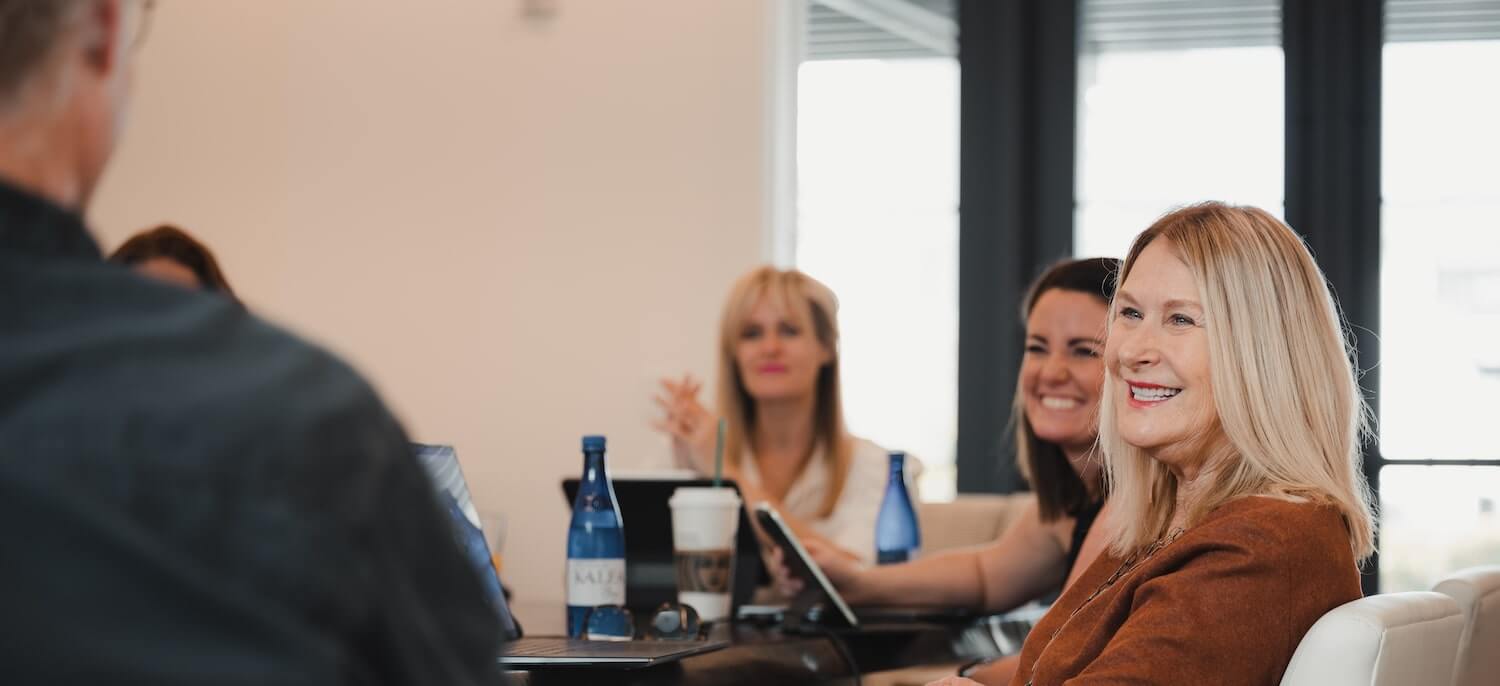 Employees in a meeting seated around a table and smiling.