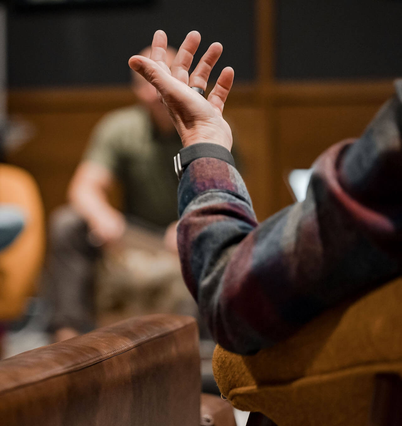 An employee with their hand up as they make a point during a meeting.