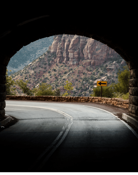 View of a road through a dark tunnel emerging into a bend up ahead.