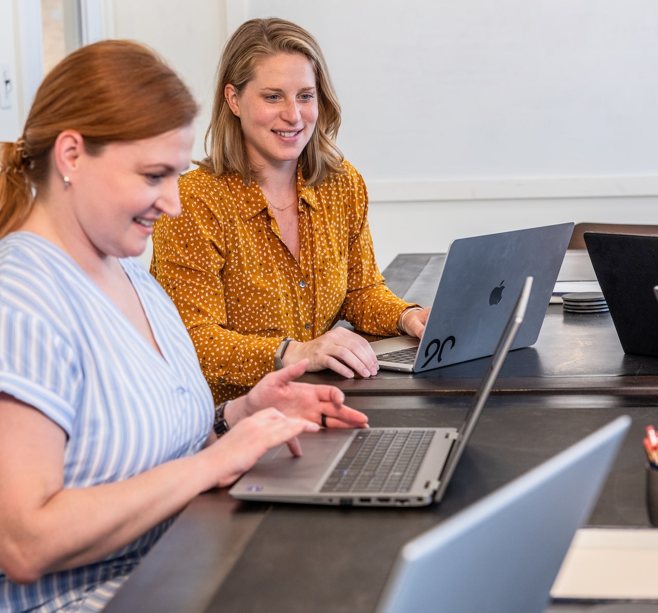 Two employees seated at a table, working on their laptops.