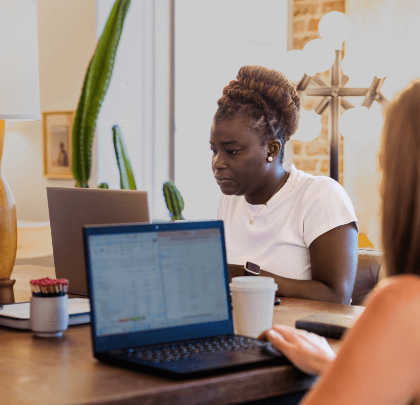 An employee working on her laptop, sitting at a table with her colleagues.