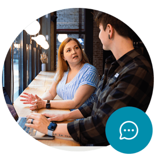 Two colleagues speaking at a cafe. Chat icon in the corner.