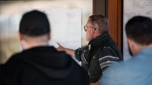 A man points to a whiteboard and others stand behind him.