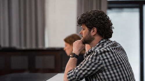 A man sits with his fist pressed on his chin.