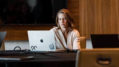 A woman sits at a table and looks at her computer.