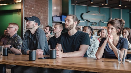 The Ninety Team sitting at tables listening intently to someone speaking/presenting.