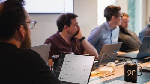 Several people sit at a table with computers in front of them