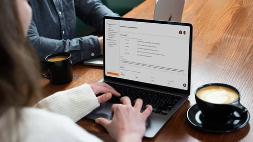 A person types on a computer. A full coffee mug sits next to the computer on a table.