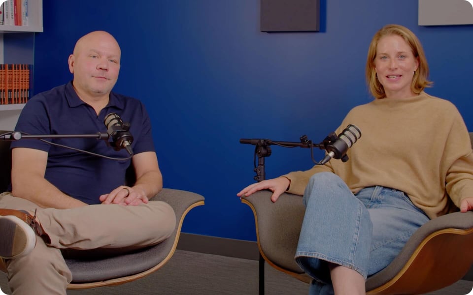 Kris Snyder and Christine Watts of Ninety sit in armchairs with microphones in a podcast studio, smiling toward the camera against a blue wall.
