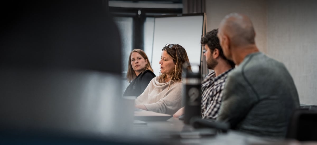 A group of people engaged in a discussion around a table, with a woman speaking in the foreground while others listen attentively. A group of people engaged in a discussion around a table, with a woman speaking in the foreground while others listen attentively.