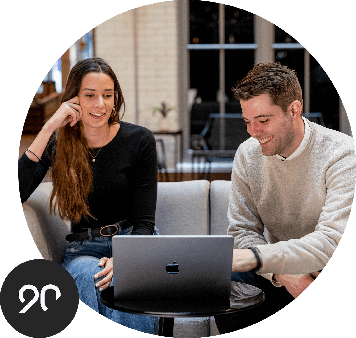 Two employees having a meeting using a shared laptop. Superimposed is the Ninety logo.