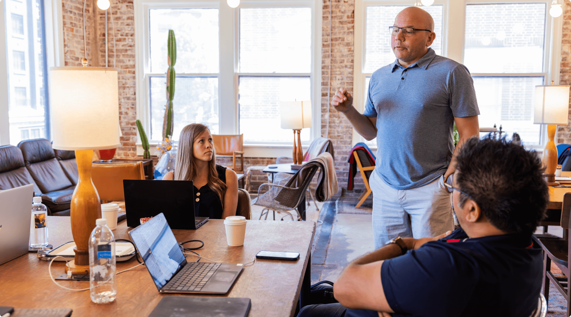Three employees having a discussion around a table. One employees is standing and leading the discussion.