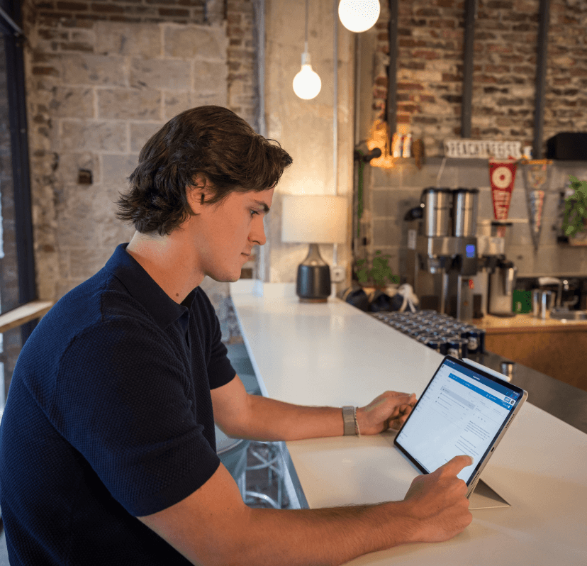 An employee sitting at a coffee bar working on a tablet.