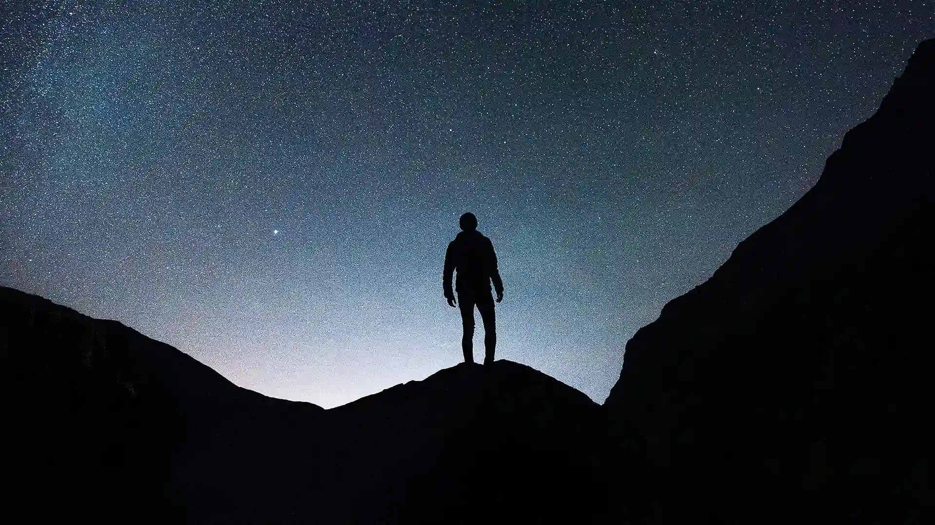 man standing on a mountain outlined against the night sky