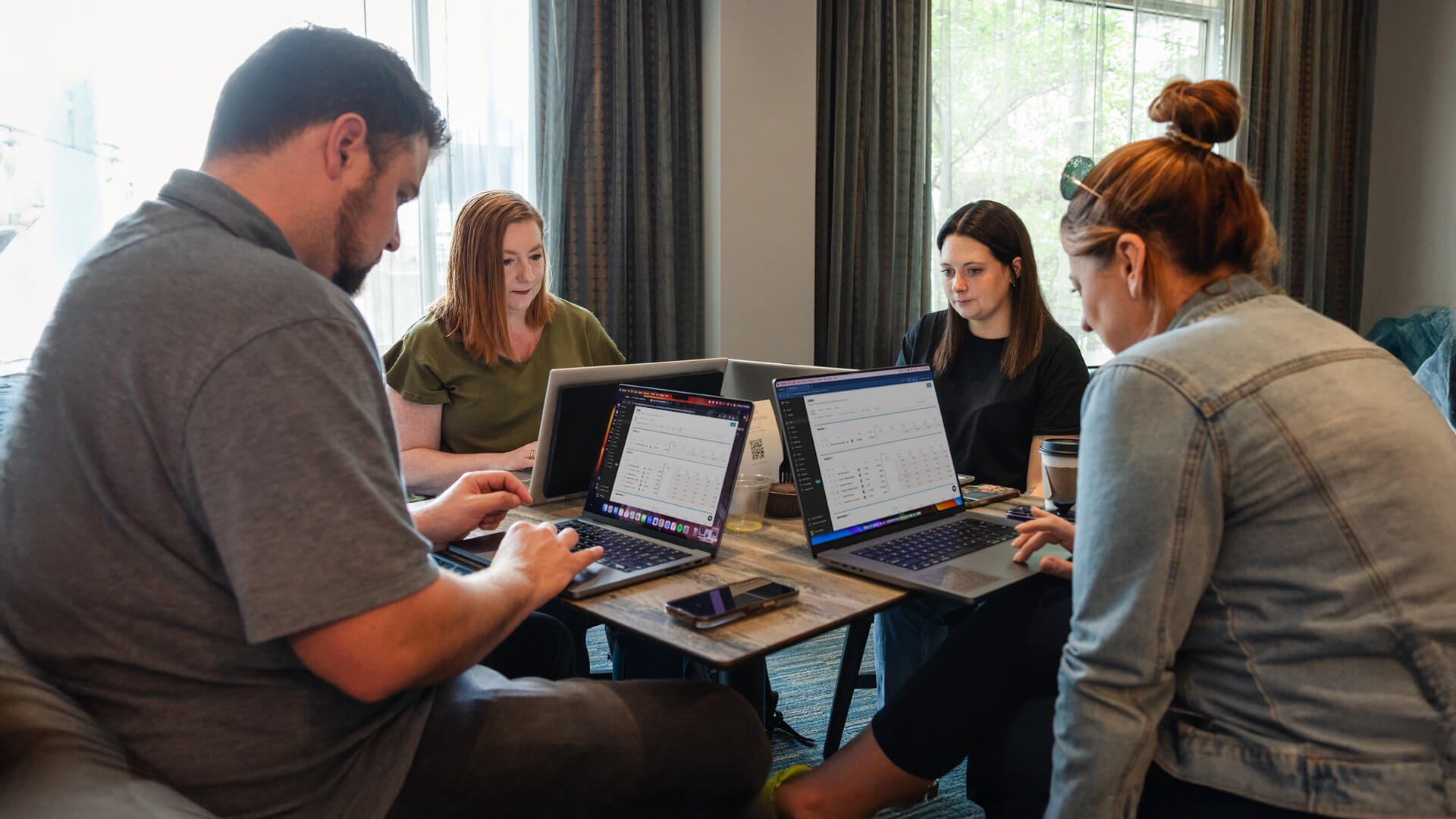Team collaborating around a conference table using business management software on laptops to track goals, manage projects, and streamline operations.