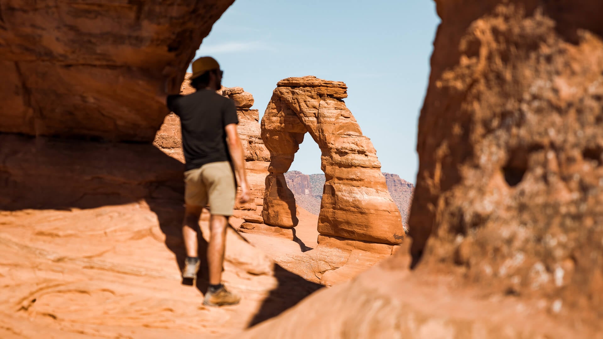 A man stands near the edge of a cliff and looks out at the sky and mountain range.