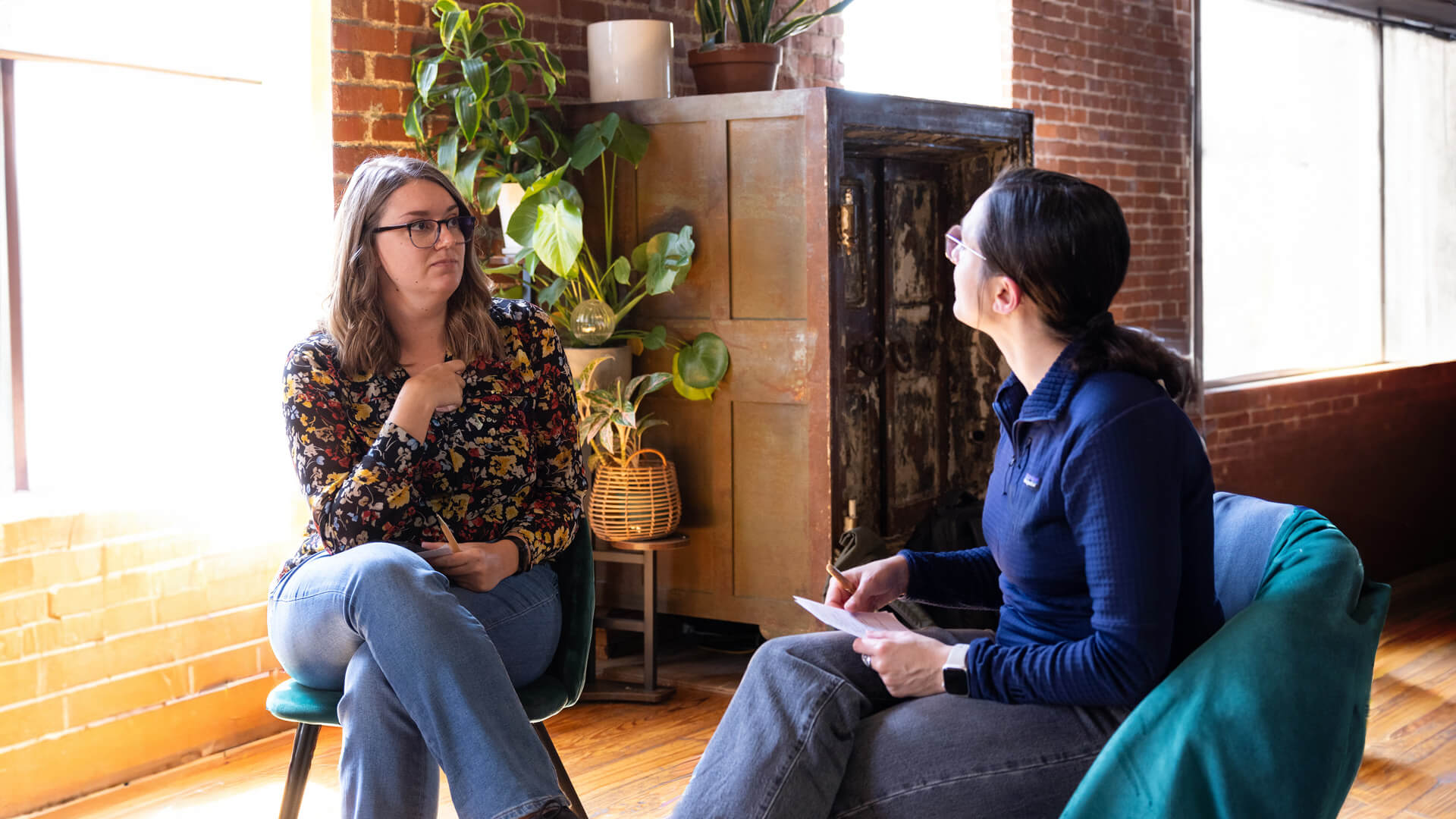 Two women sit in chairs facing one another.