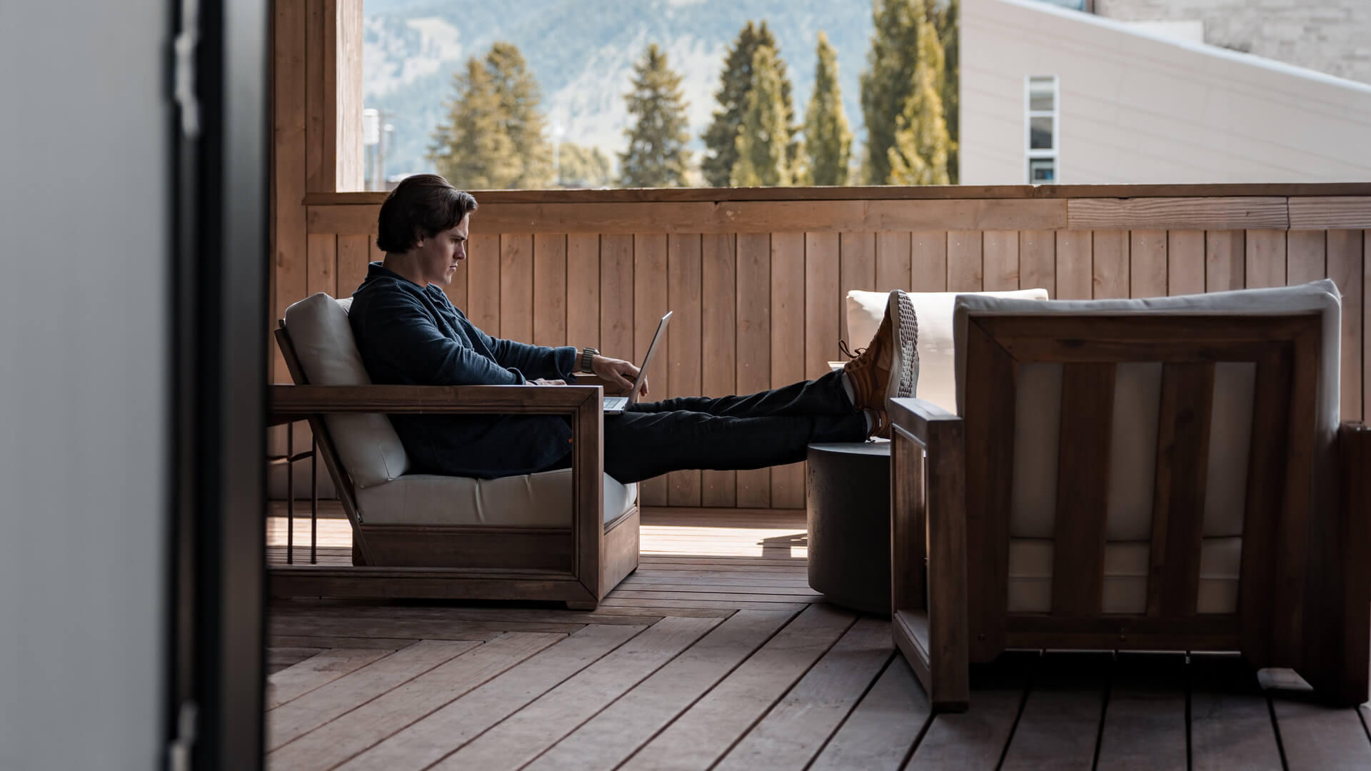A man sits on a chair with his legs out in front of him and a computer on his lap.