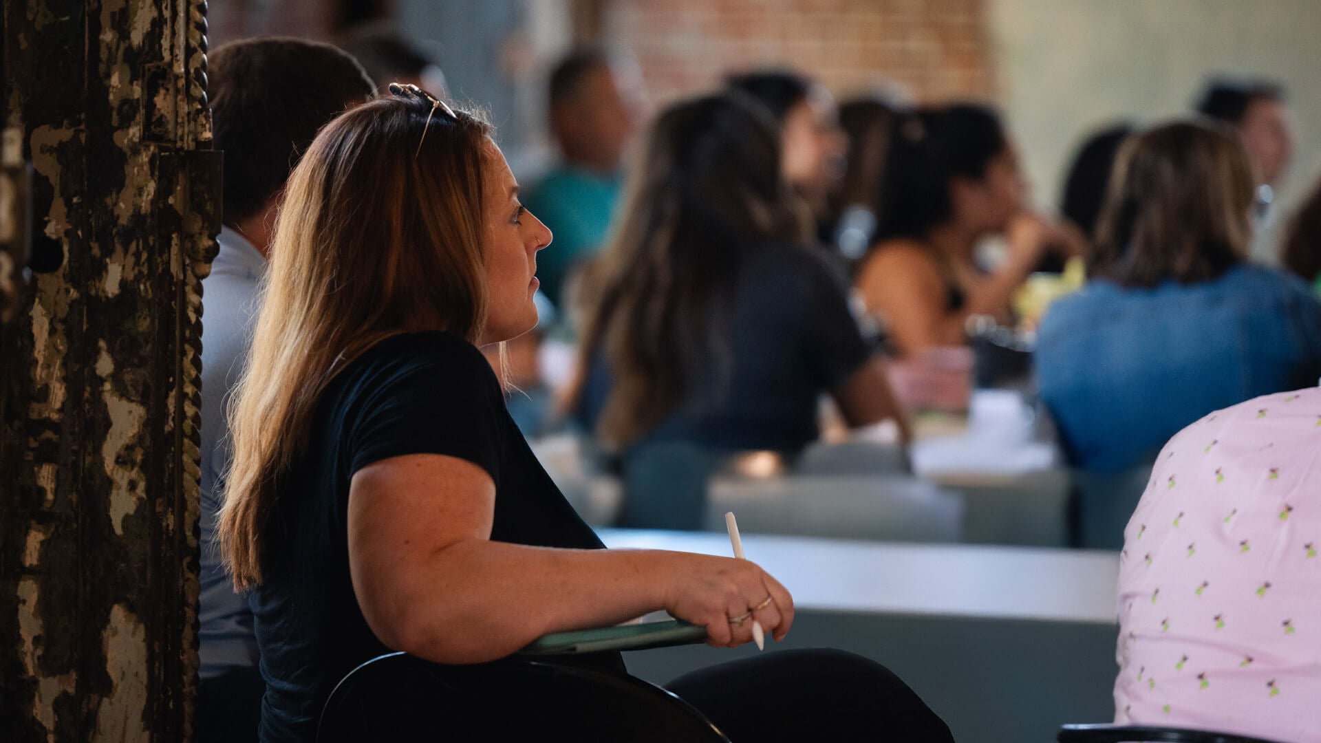 Woman sitting down at a table, listening to a speaker. 