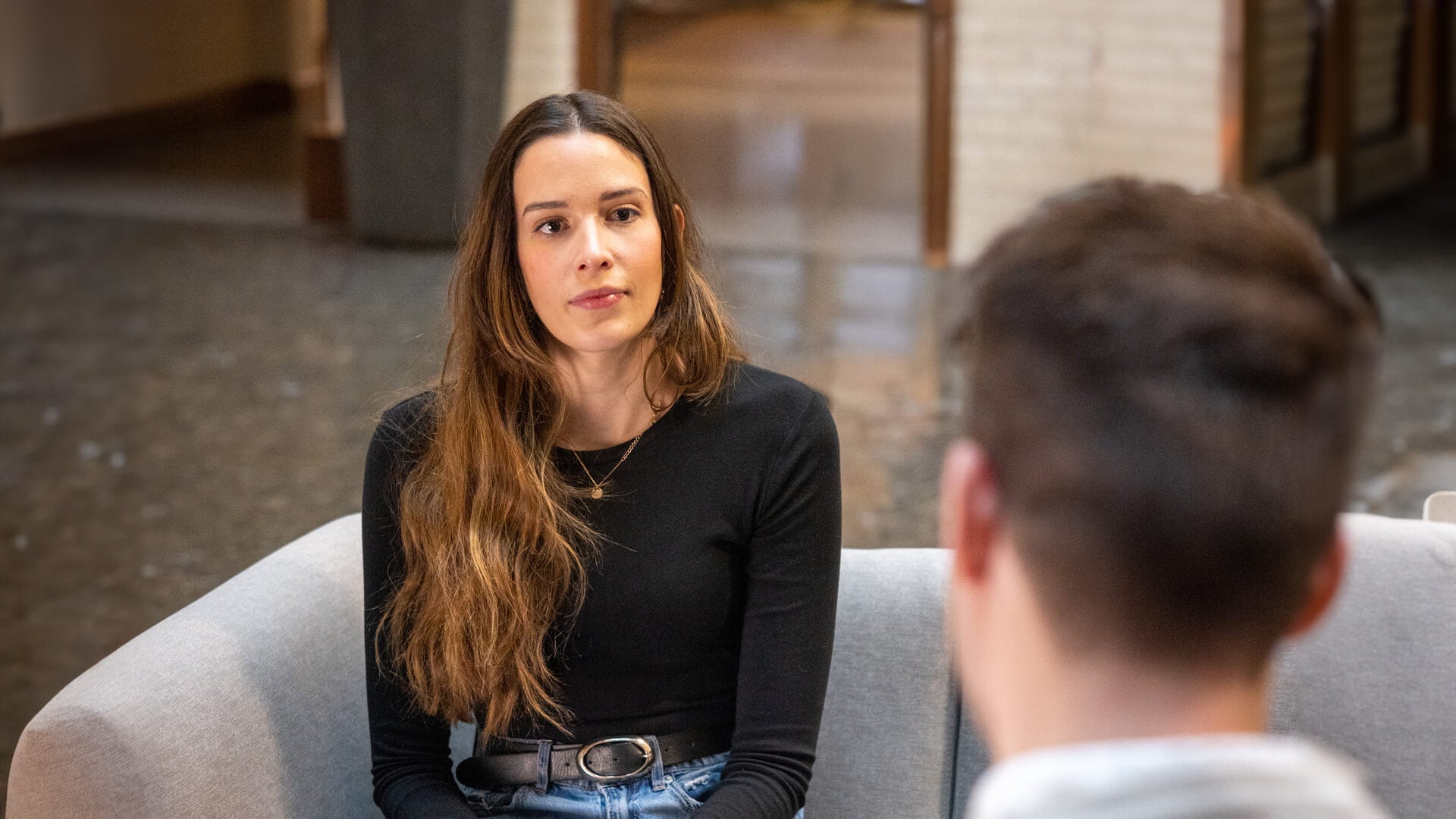 A woman sits on a couch and looks at someone who is facing her.